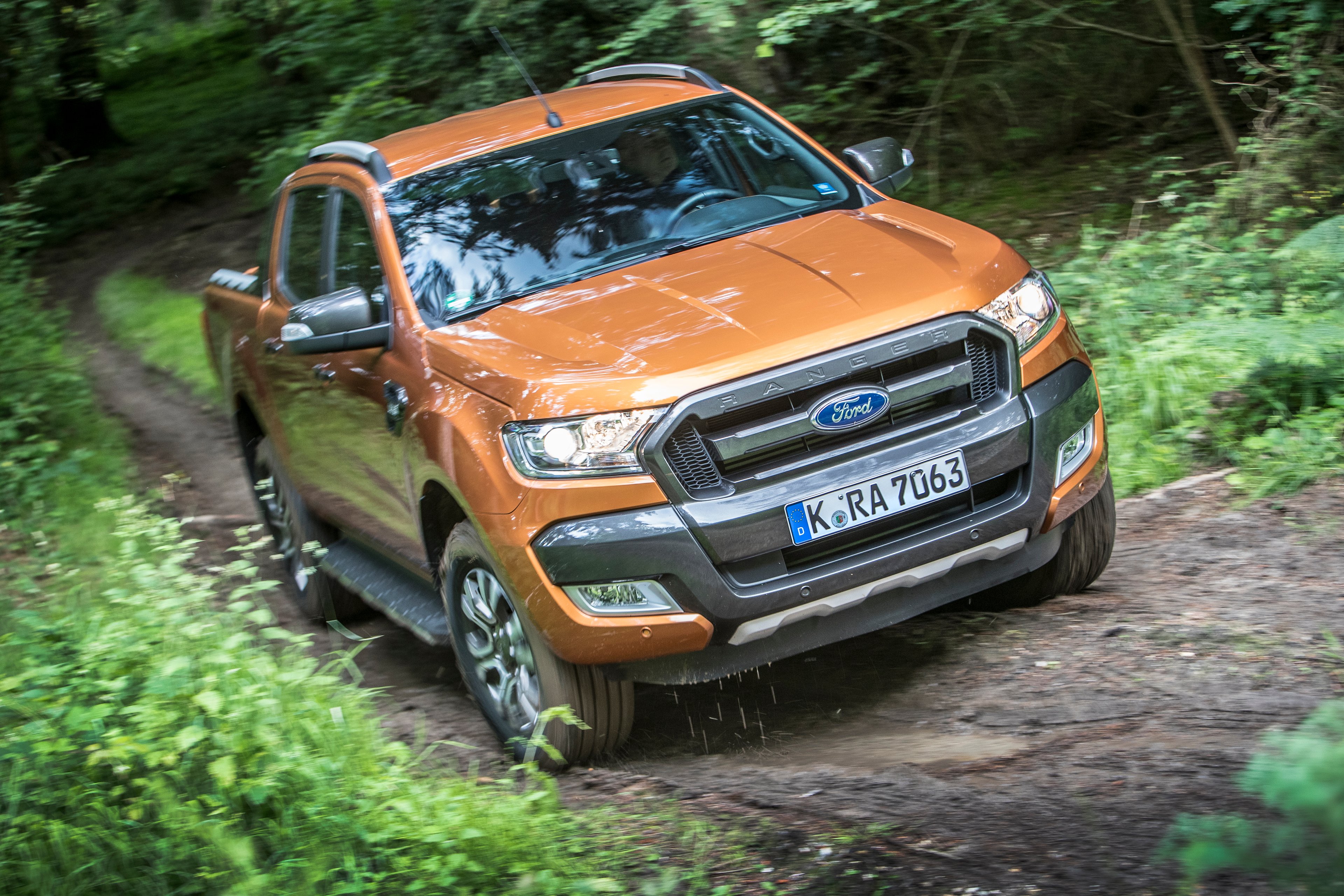 An orange 2017 Ford Ranger pickup on a dirt road in a forest, wth a European license plate.