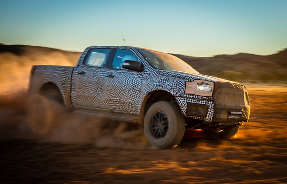 A prototype Ford Ranger Raptor, partly covered to hide its styling details, is shown moving at high speed across a desert landscape in Australia.