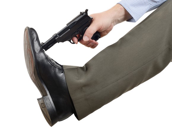 A man pressing a revolver against his shoe as if to shoot it