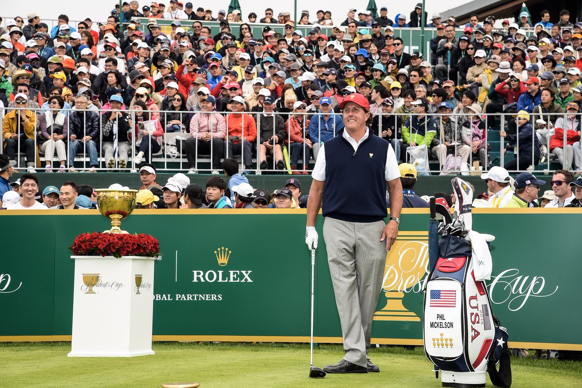 Phil Mickelson stands holding a club in front of fans in bleachers.