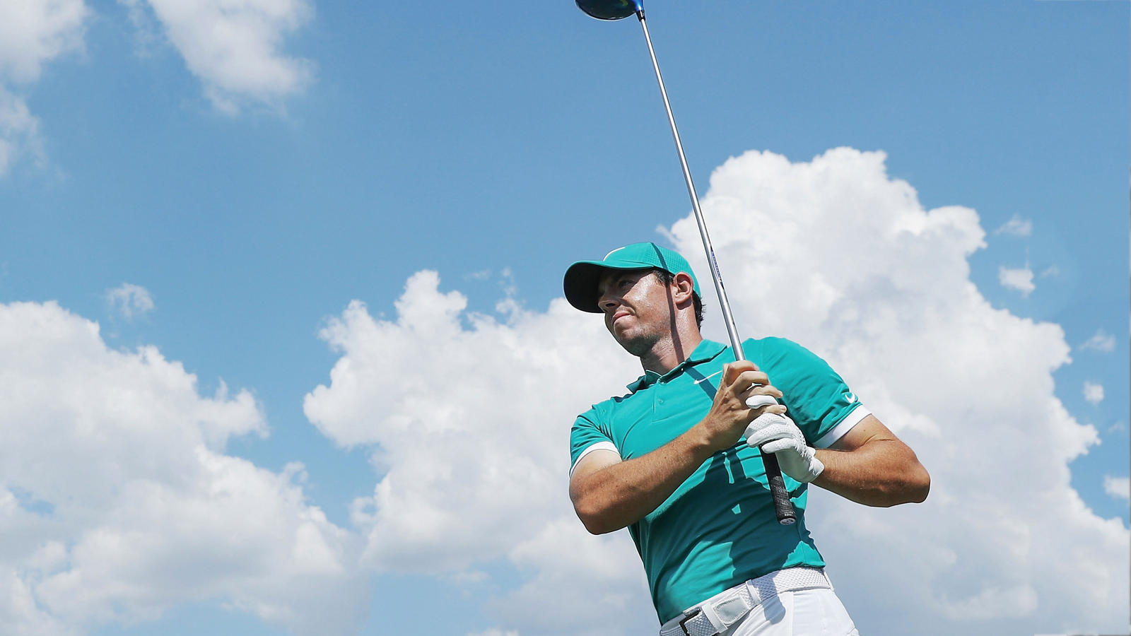 Rory McIlroy holds a golf club in front of him with the sky as a background.