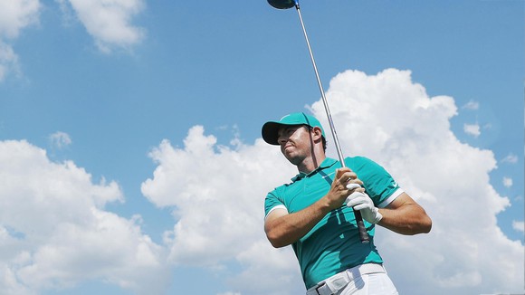 Rory McIlroy holds a golf club in front of him with the sky as a background.