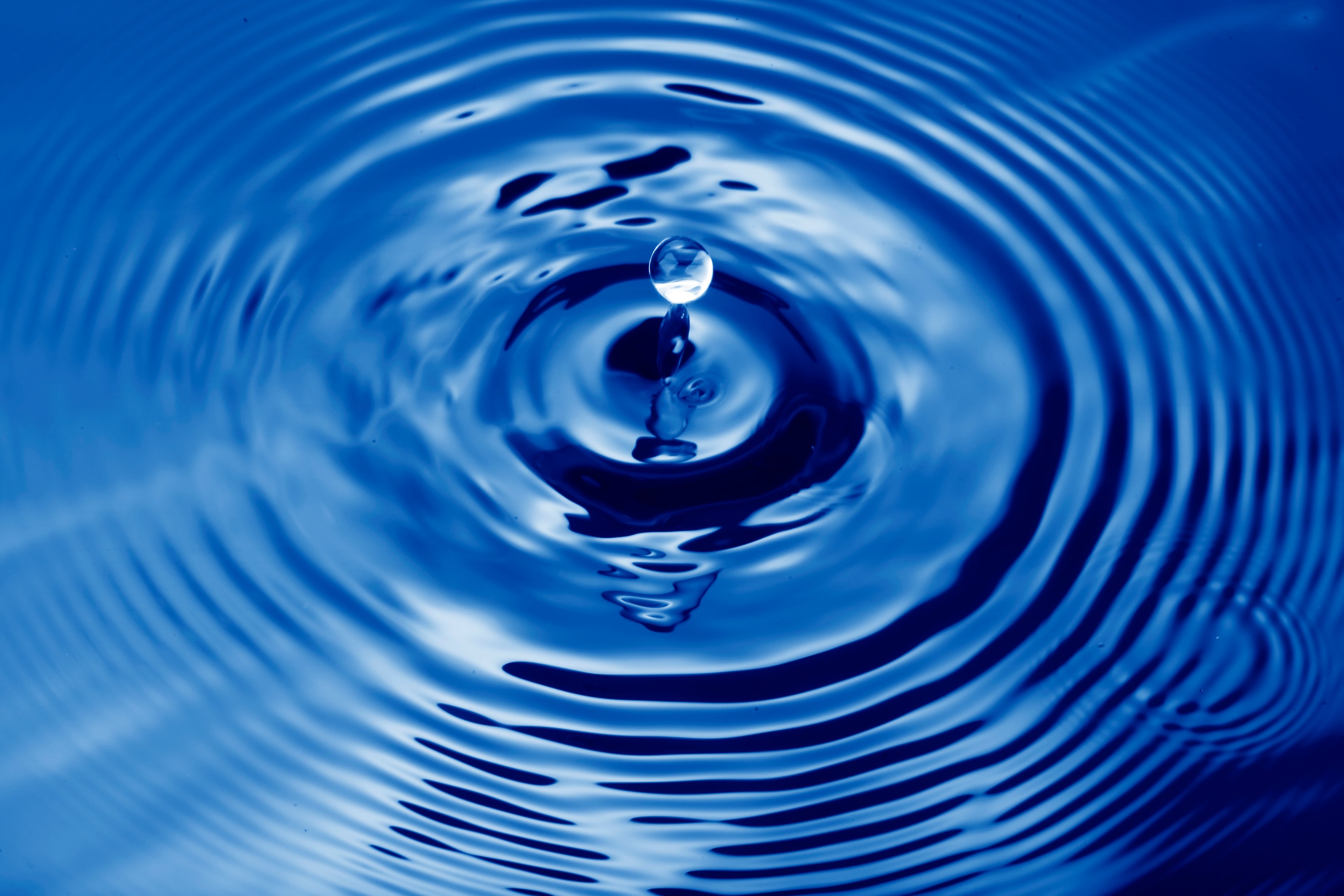 Water drop falling on body of water causing ripples.