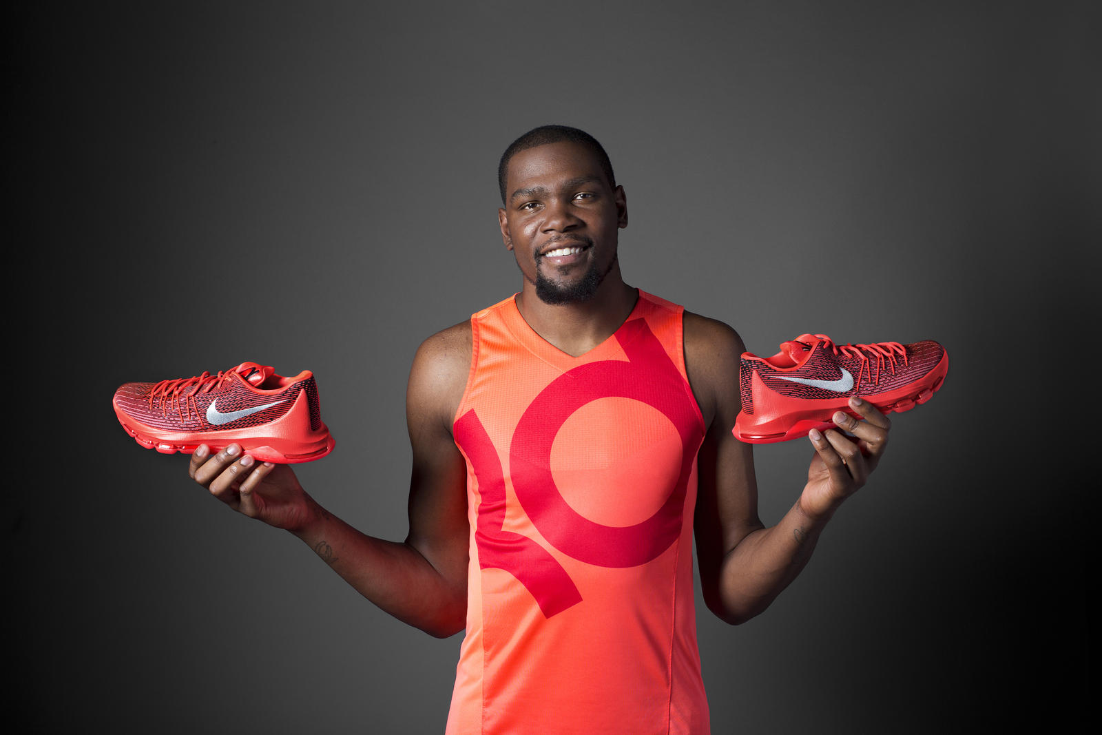 NBA star Kevin Durant holding a pair of his signature Nike shoes in red and orange.