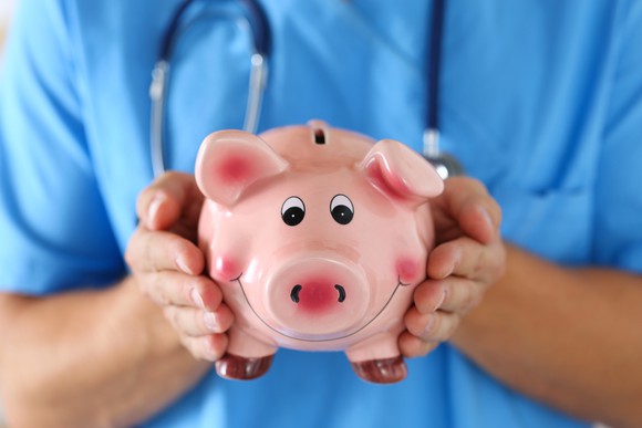 A doctor holding a smiling piggy bank.