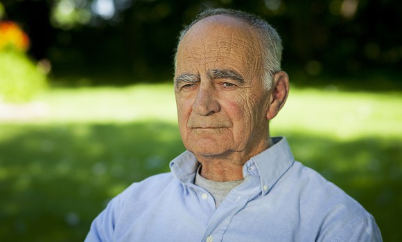 An elderly man sits outdoors with a concerned expression.