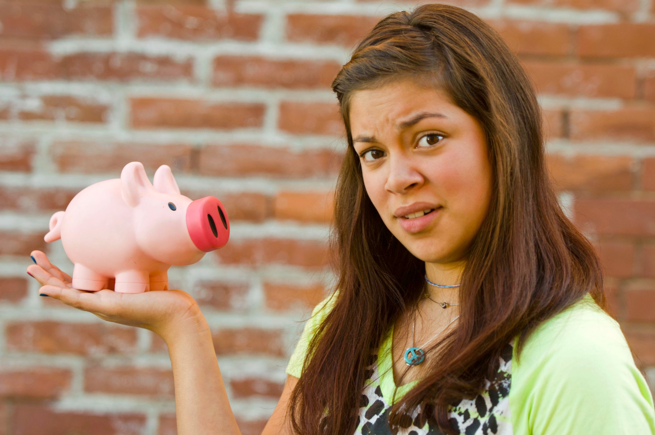 A young woman with a confused look holding a piggy bank. 
