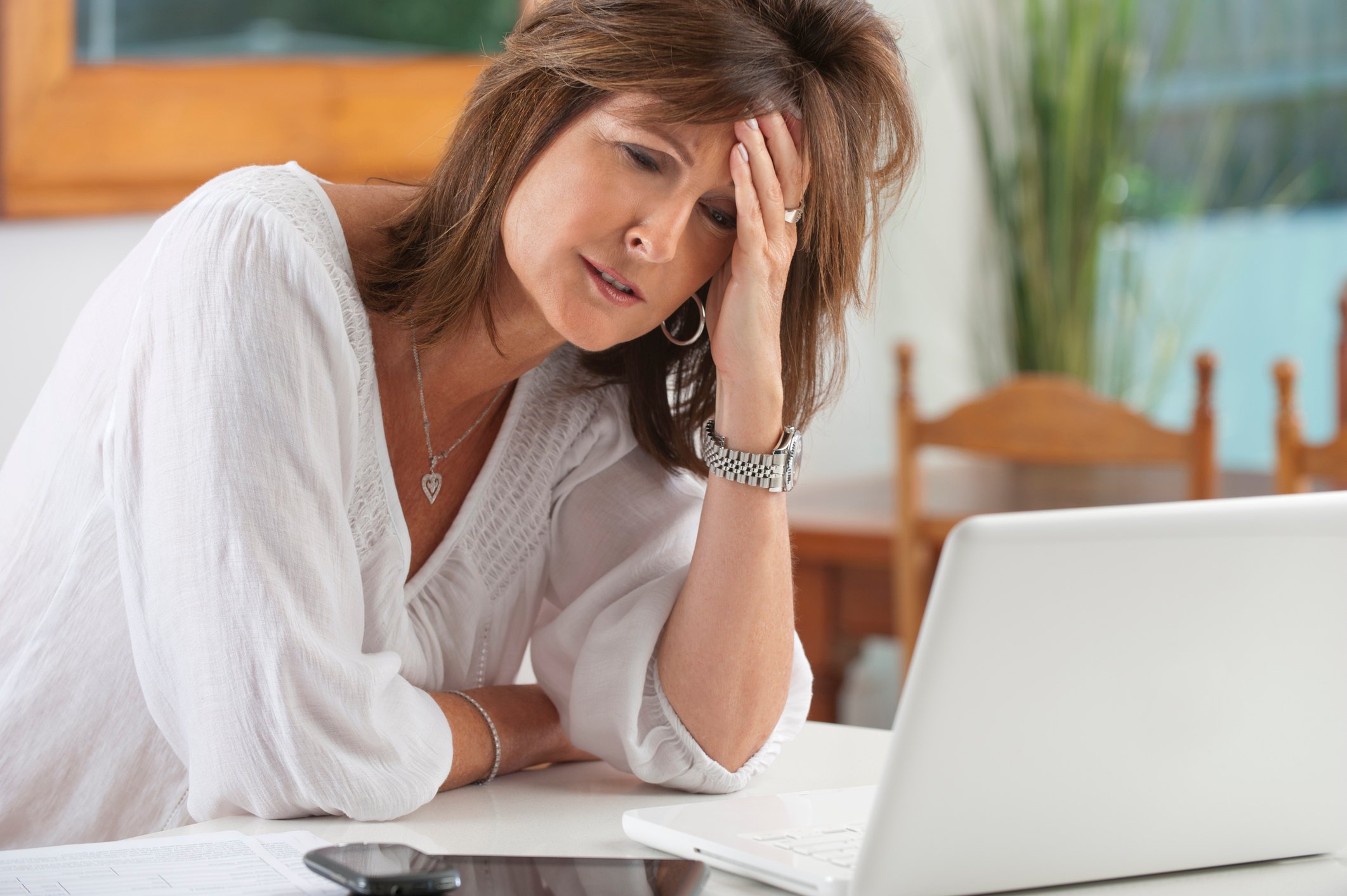 A frustrated woman holding her head in her hand in front of her laptop.