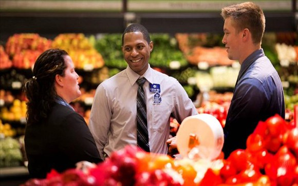 A Kroger employee talks with two people in the produce section.