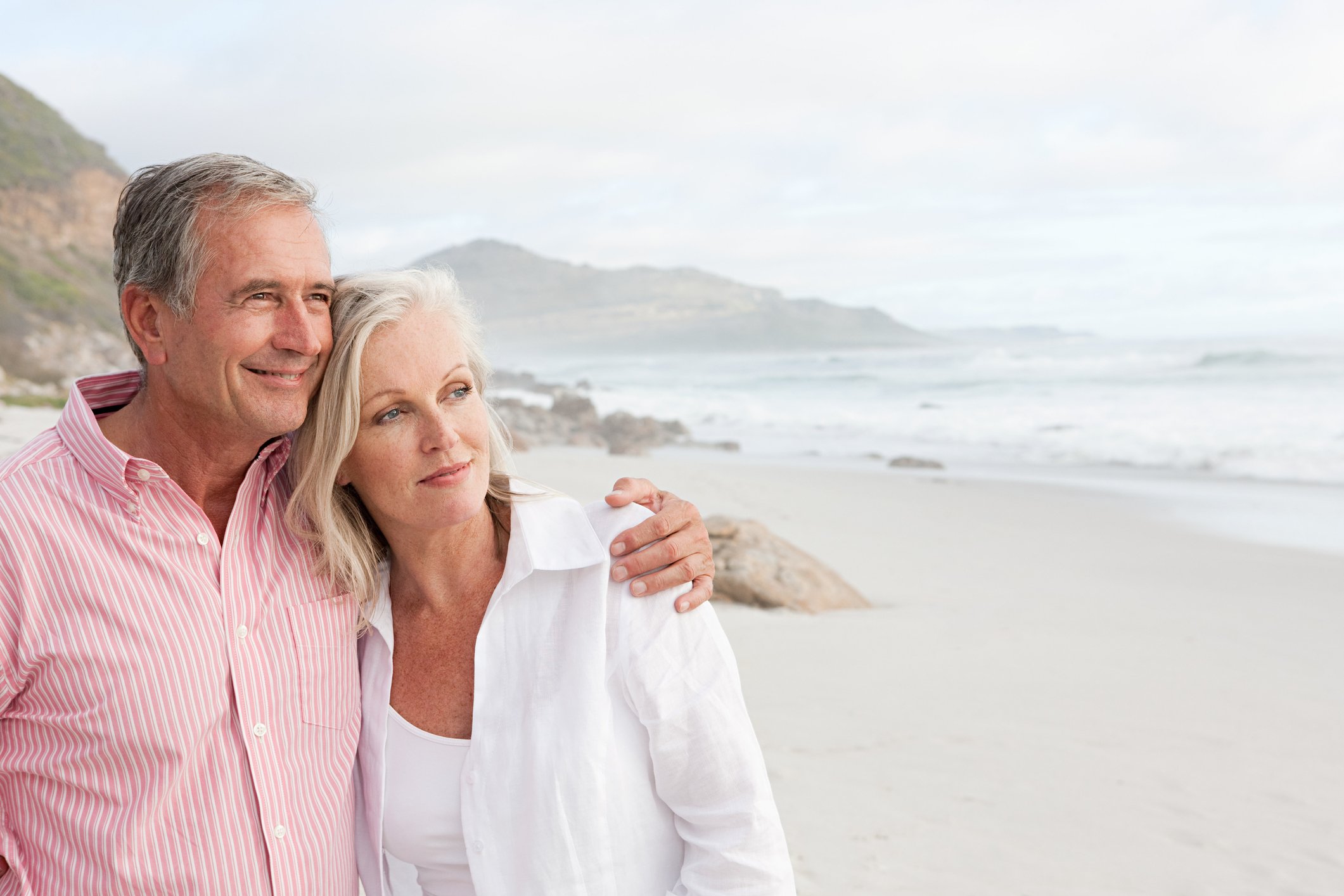 Older couple on a beach, looking at the ocean.