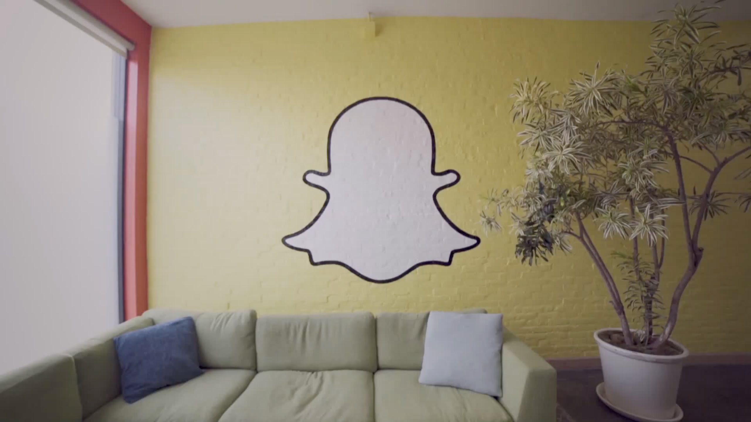 Yellow wall decorated with a white Snapchat ghost. A green couch and a potted plant can also be seen.