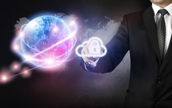 Businessman holding out his hand towards a digital image of a glowing Earth, surrounded by strands of brighter lights. Between his fingers, he holds a digital icon of a padlock inside a cloud.