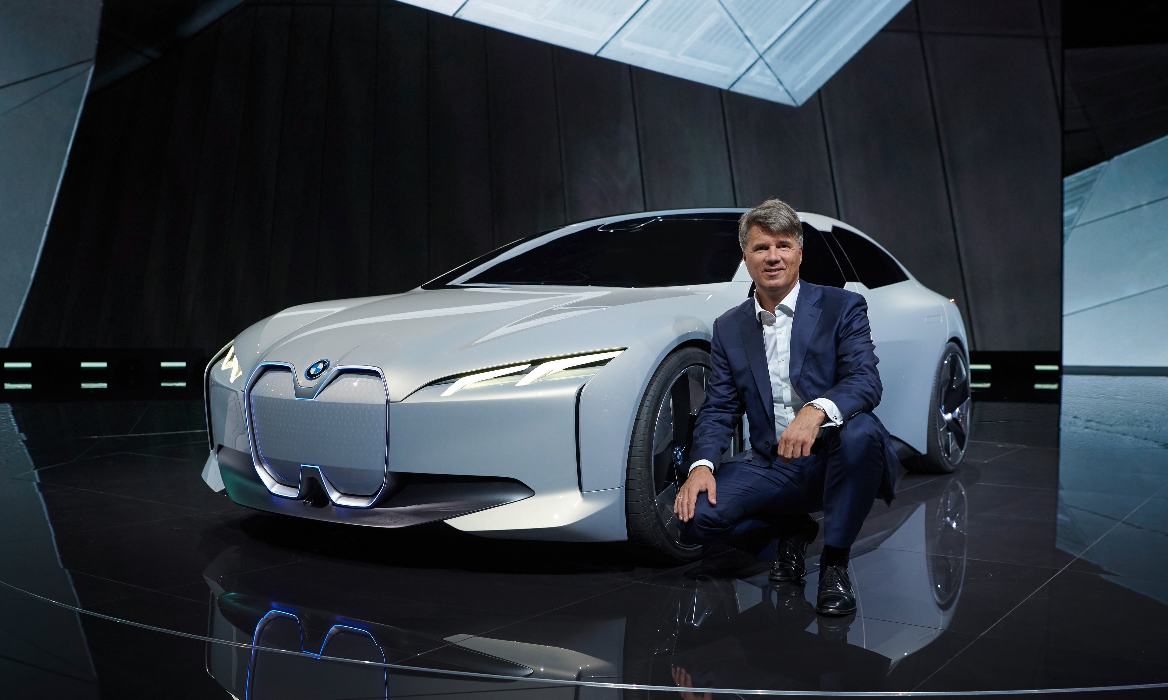 BMW CEO Harald Krueger is squatting next to the i Vision Dynamics, a sleek-looking white sedan.