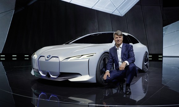 BMW CEO Harald Krueger is squatting next to the i Vision Dynamics, a sleek-looking white sedan.