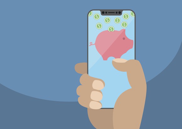A hand holding a smartphone displaying a piggy bank with cash.