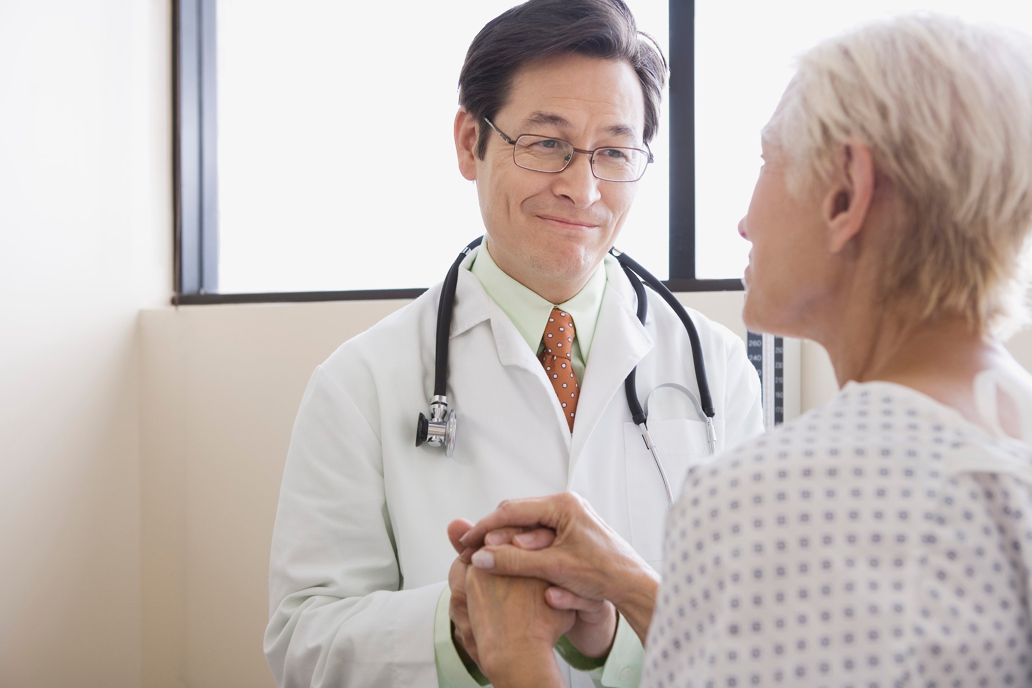 A smiling male physician holding the hand of a senior female patient. 