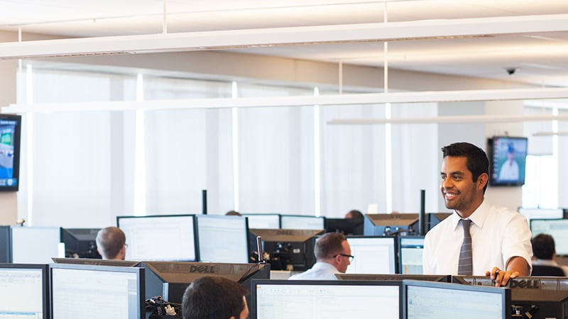 Goldman Sachs employee standing up in a room of double-monitor workstations.