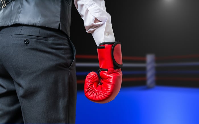 A businessperson standing in a boxing ring wearing a boxing glove.