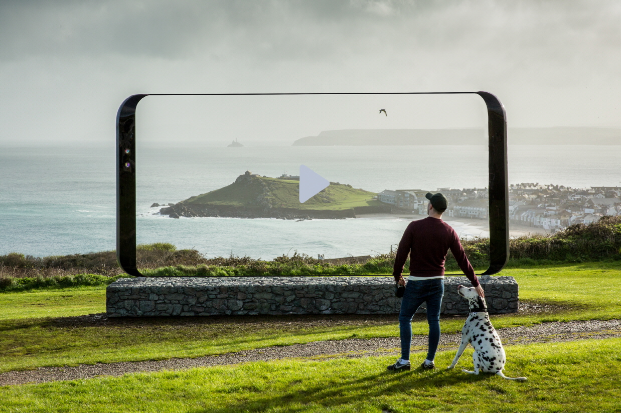 A man and a dalmatian standing in front of an oversized Galaxy S8 featuring an image that blends perfectly with the surrounding landscape.