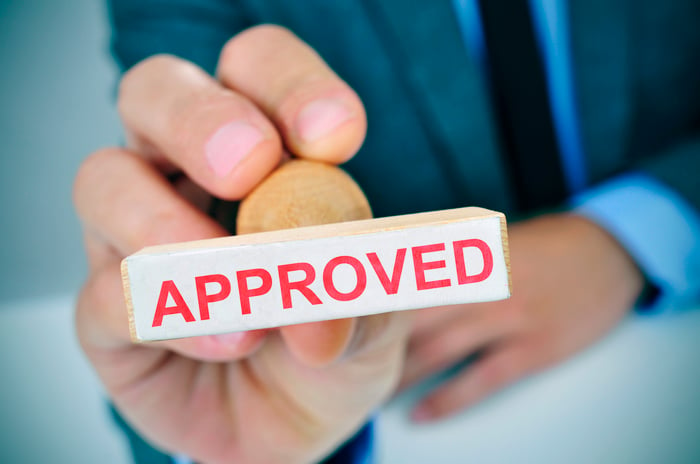 A person holds a rubber stamp that reads "Approved."