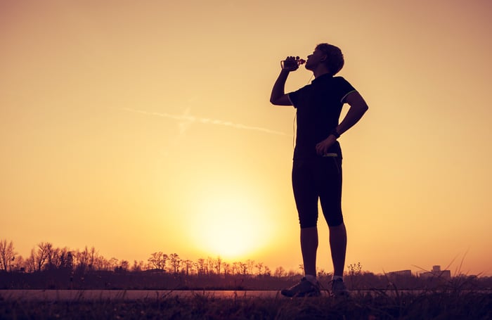 Runner stopped to drink water with sun on horizon in background