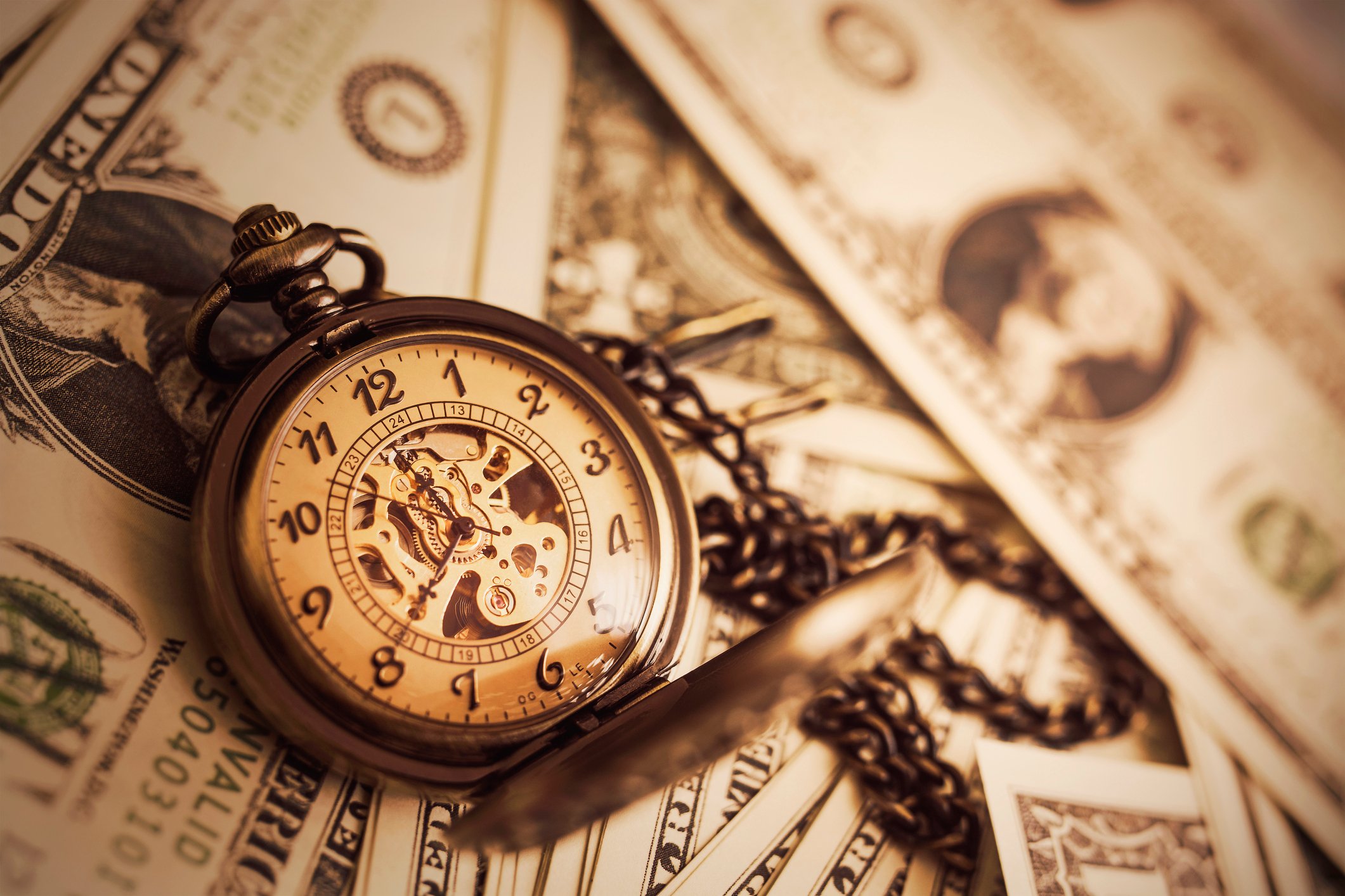 An antique pocketwatch with chain, sitting on top of dollar bills