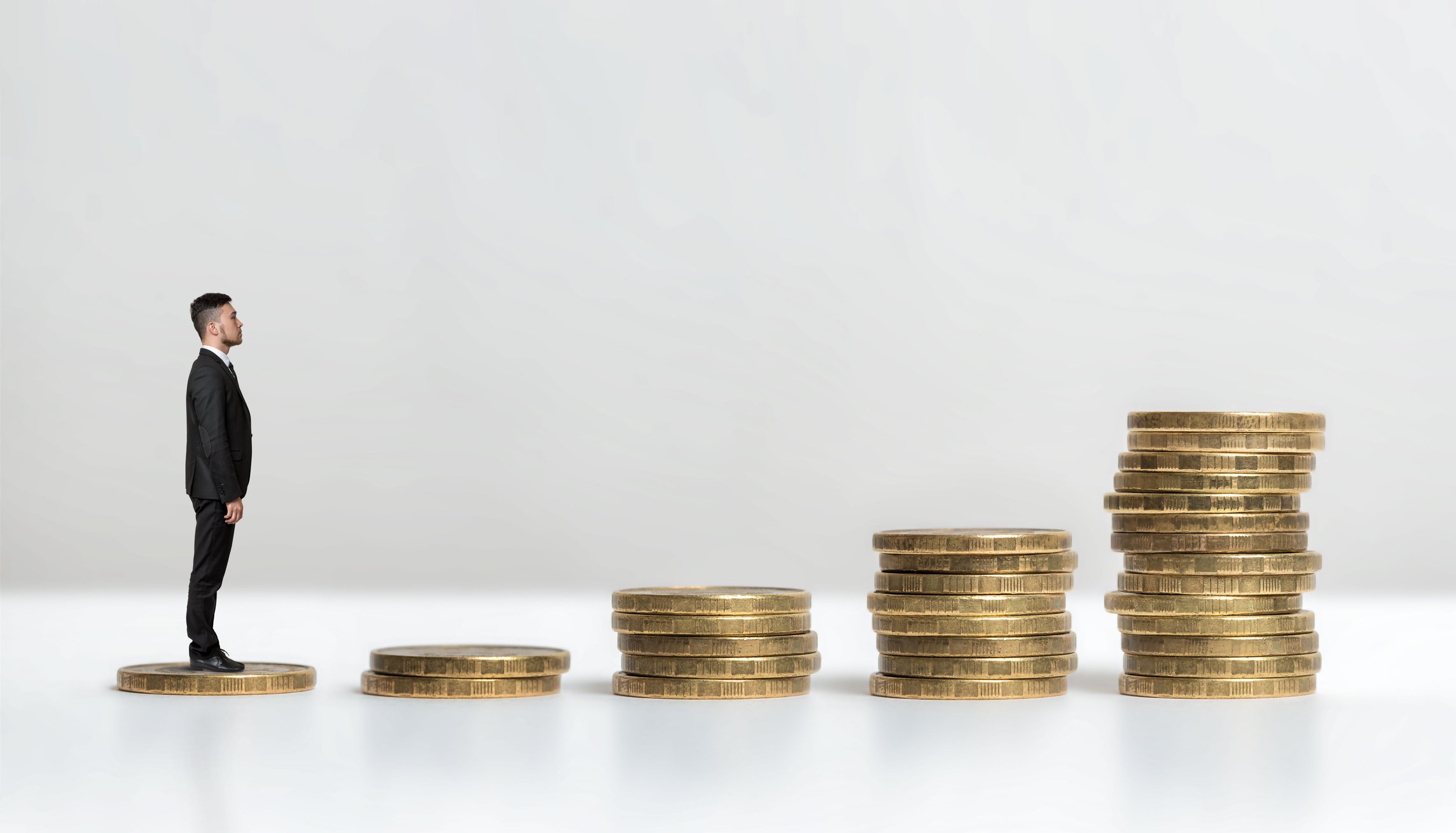A miniature man walking up steps made of coins