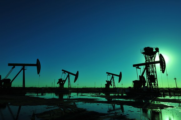 Oil wells in silhouette at night in a wet landscape.
