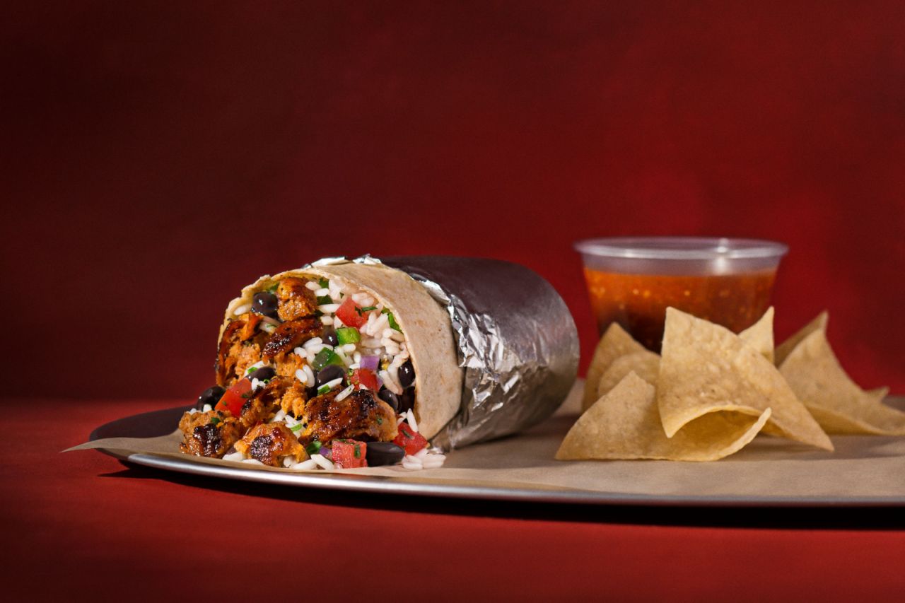 A chorizo burrito on a plate with a side of chips and salsa.