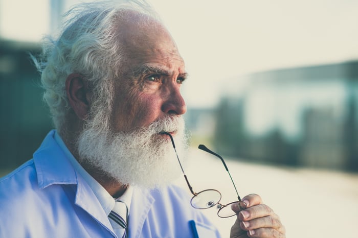 An elderly man thinking while holding part of his glasses between his lips