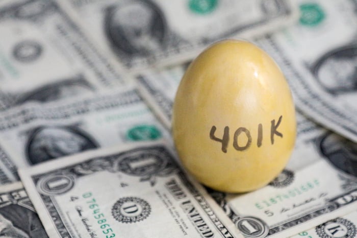 A golden egg with "401k" written on it, sitting on a pile of cash.
