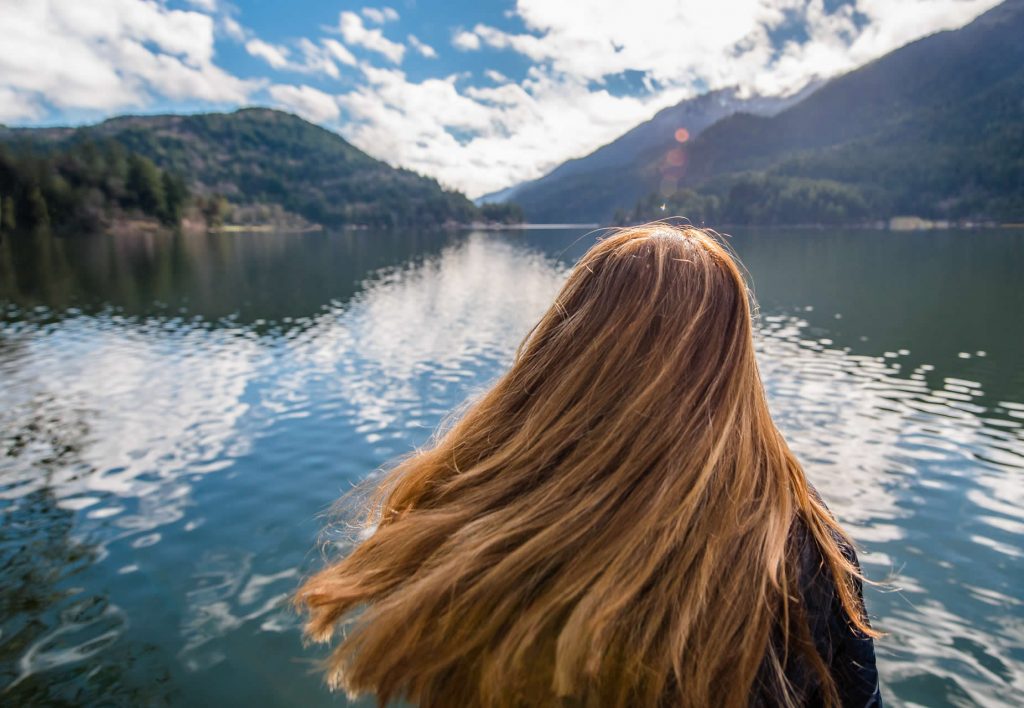 A long-haired woman looking out over a lake.