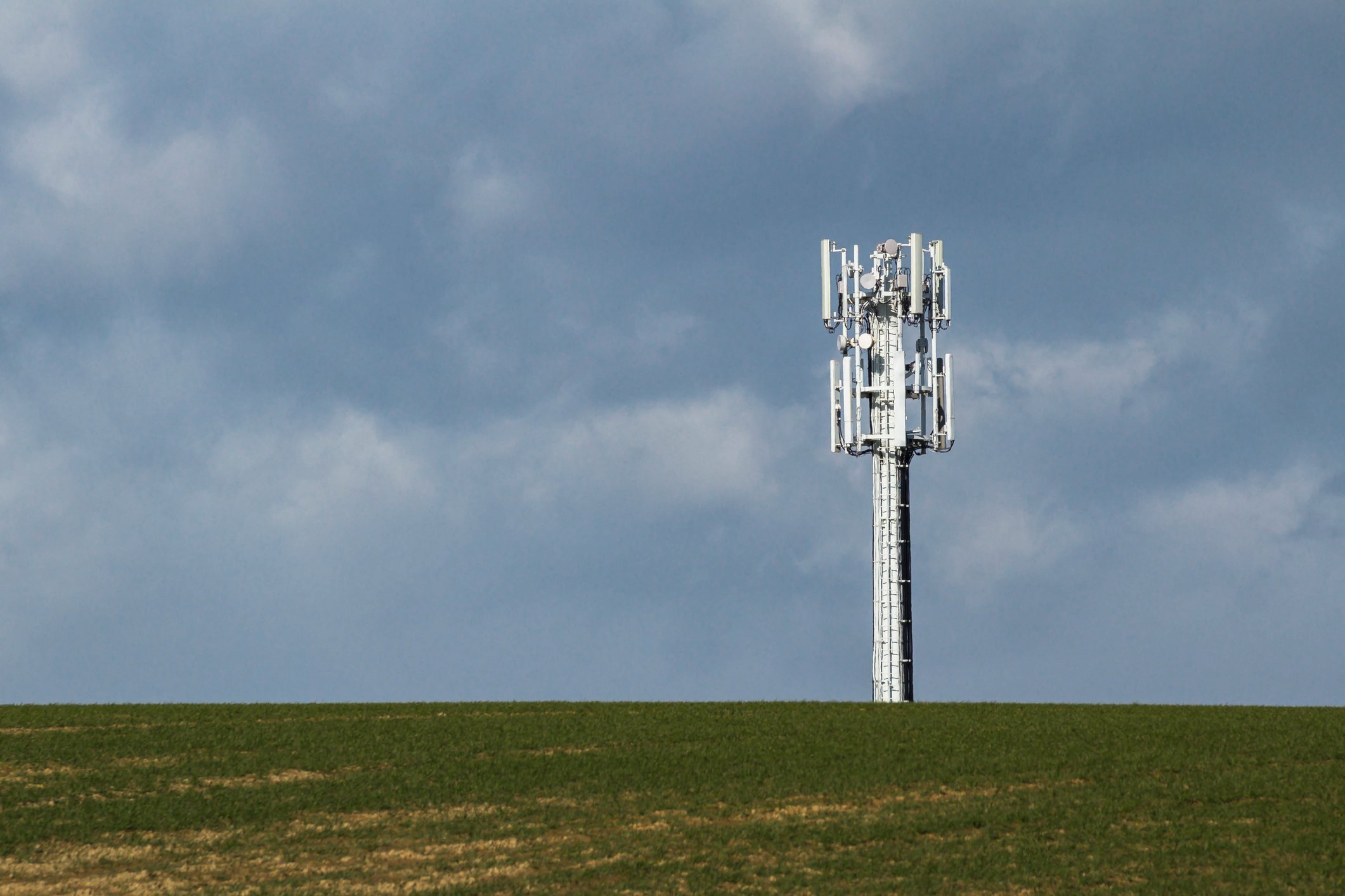 A cellphone tower at the top of a hill with a cloudy sky in the background.