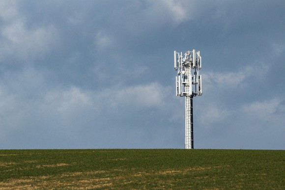 A cellphone tower at the top of a hill with a cloudy sky in the background.