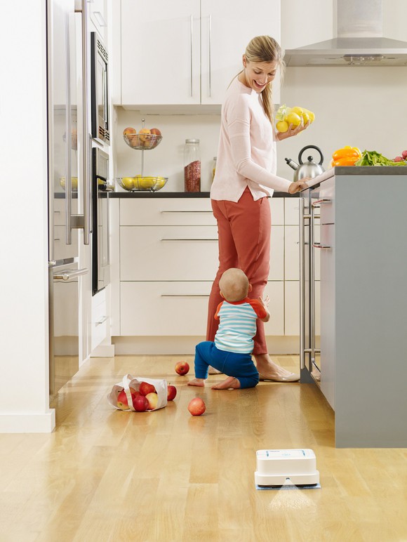 iRobot Braava cleaning a kitchen floor while a mother and child play in the background.