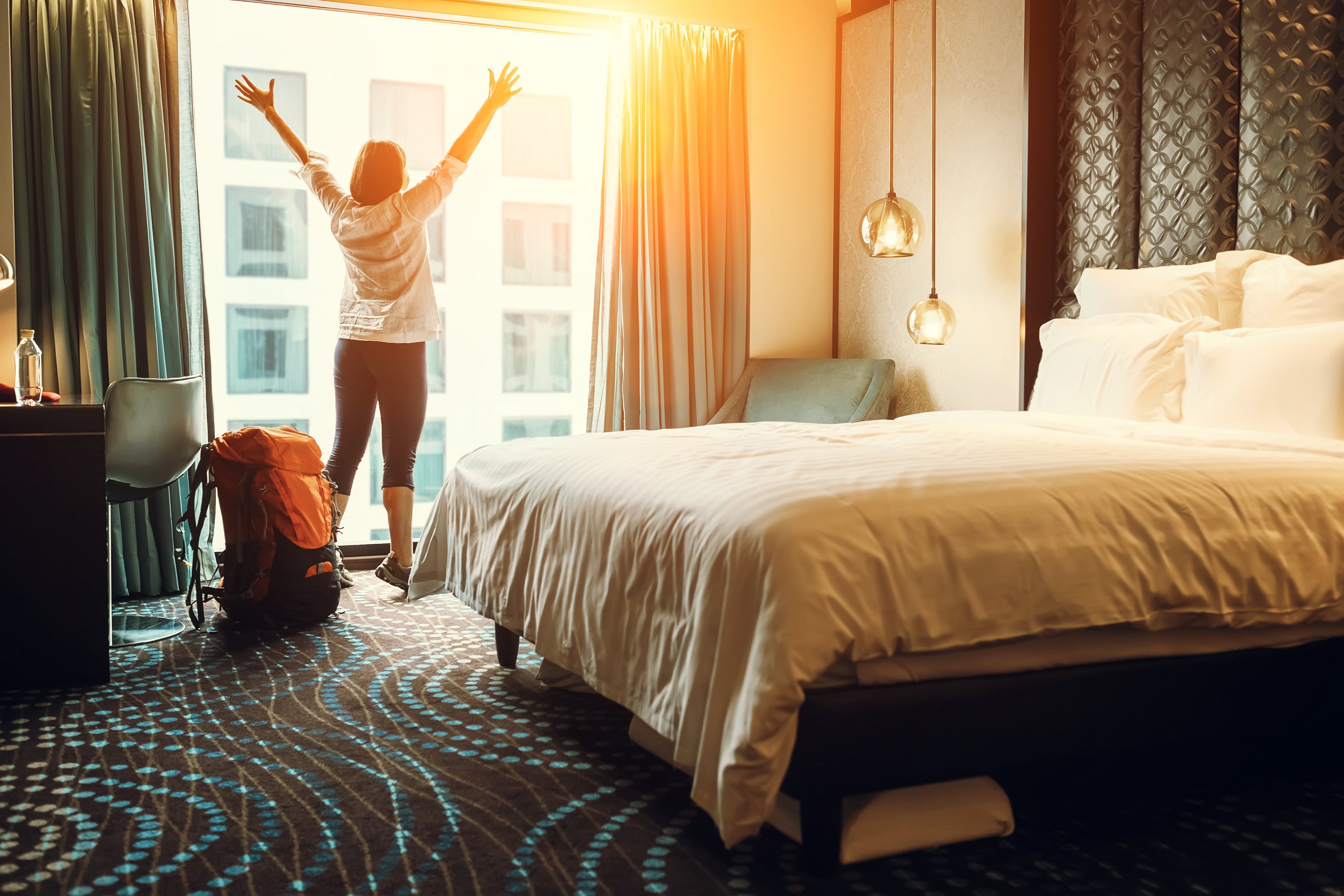 A woman lifts her arms and stretches inside a hotel room