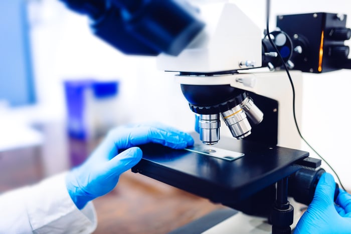 A biotech lab researcher examining a sample with a microscope. 