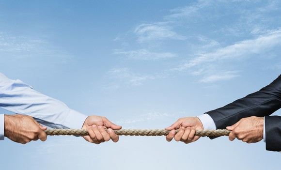 Two pairs of hands in business attire engage in a Tug of War.