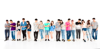 Numerous young people lined up looking at phones.