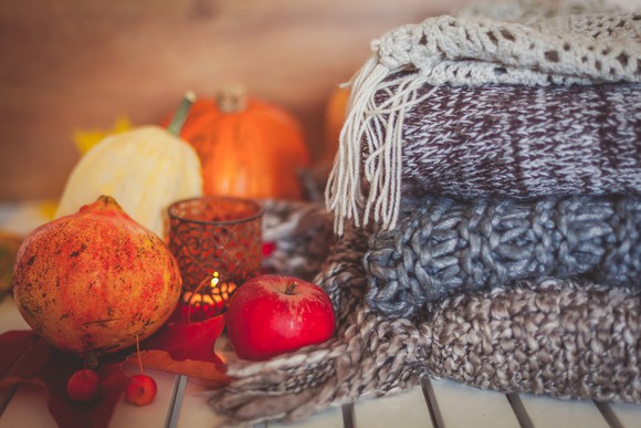 Gourds and pumpkins next to a candle, apple, and pile of blankets
