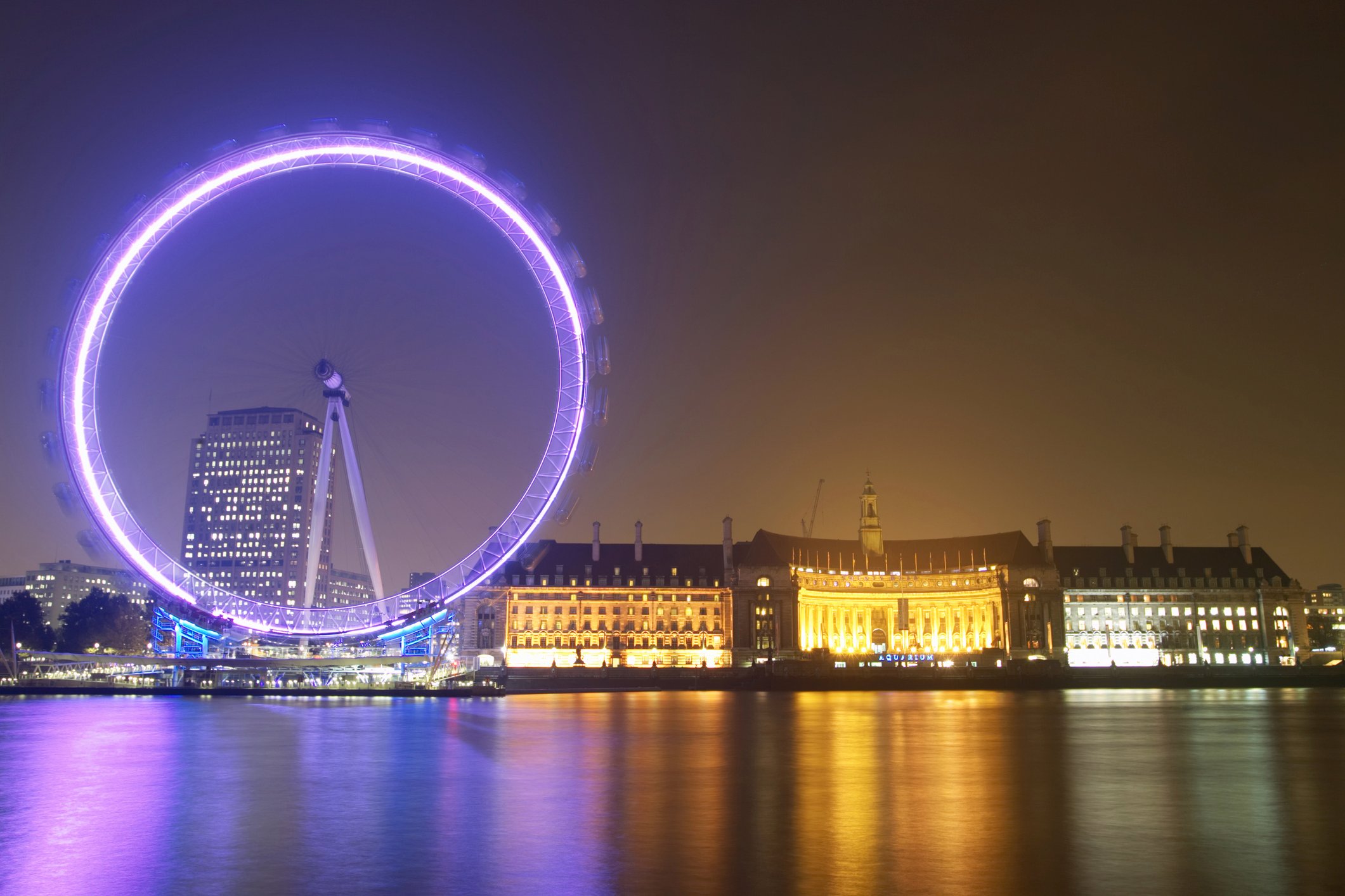 The London Eye ferris wheel lit up at night with part of the London skyline.