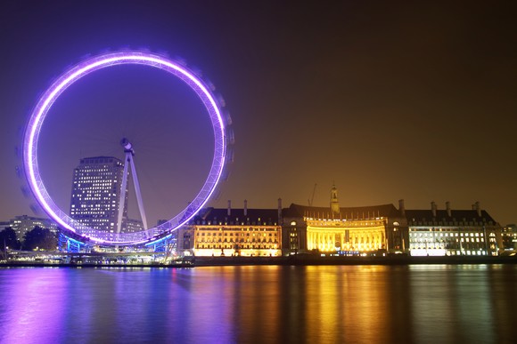 The London Eye ferris wheel lit up at night with part of the London skyline.