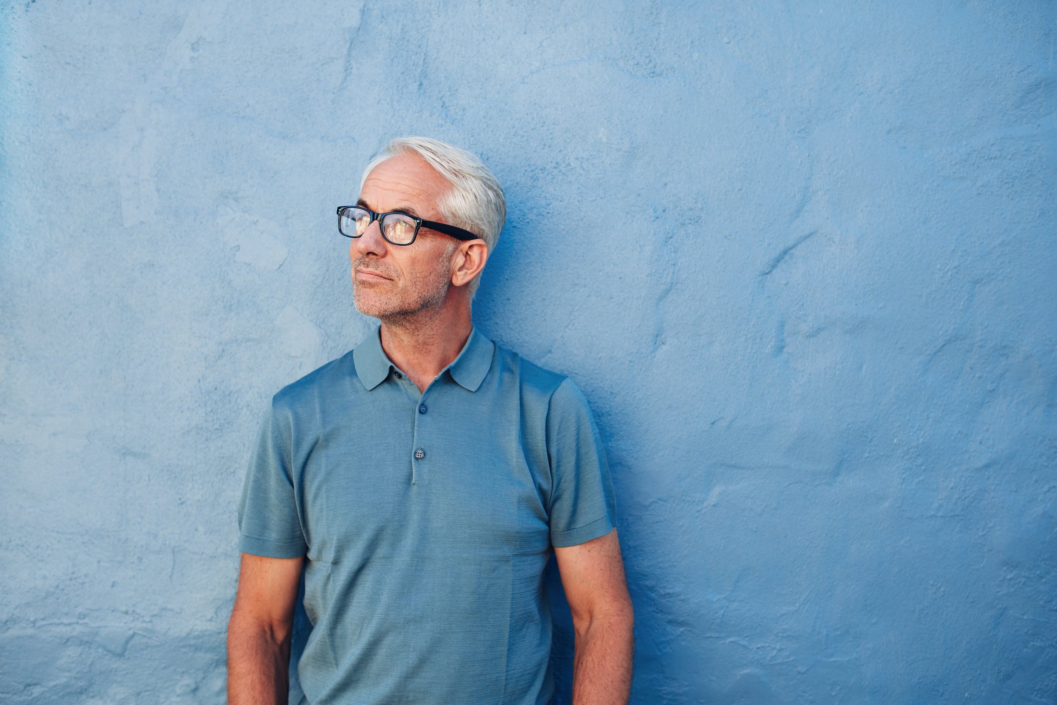 Older man wearing eyeglasses standing against a blue background