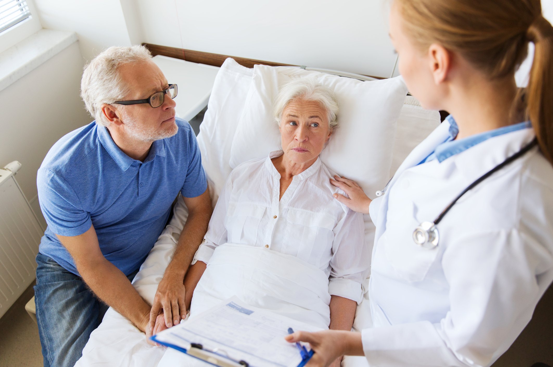 Senior woman in hospital bed and senior male at her side talking to doctor