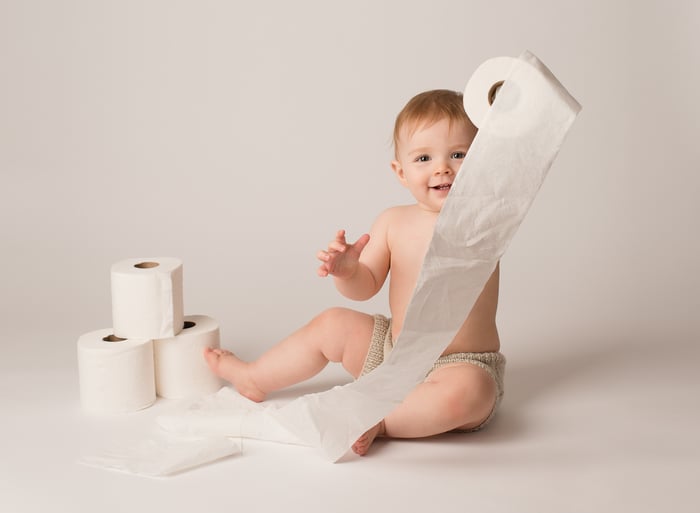 A baby sitting on the floor and playing with a roll of tissue paper.