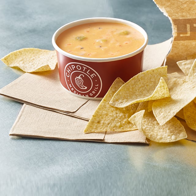 A cup of Chipotle's queso with chips on the side