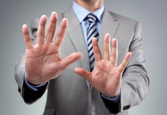 A man in a suit putting his hands up as if to say "no thanks."