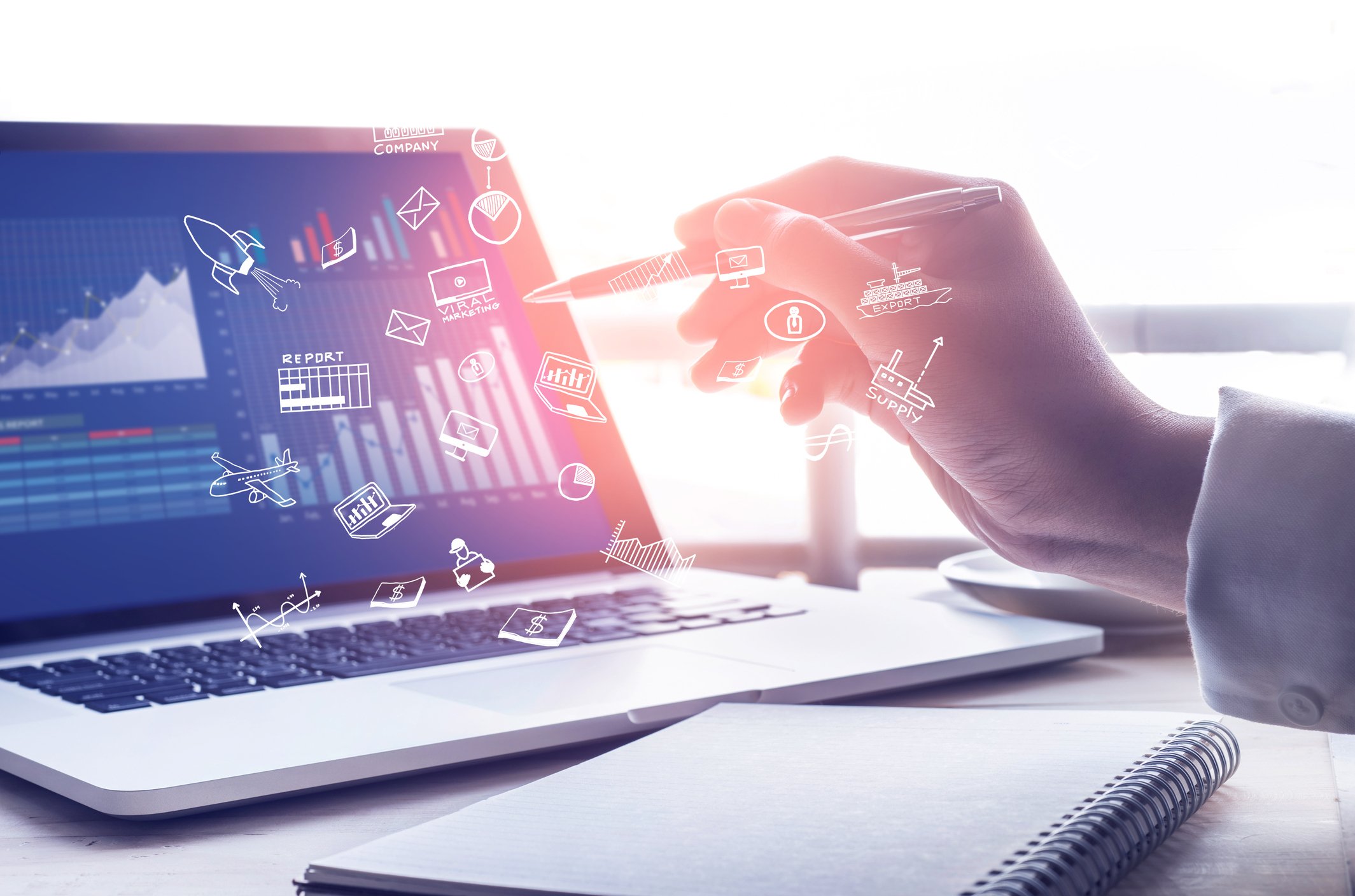 A hand holding a pencil points to a laptop screen on a desk, with various icons coming out of the screen.