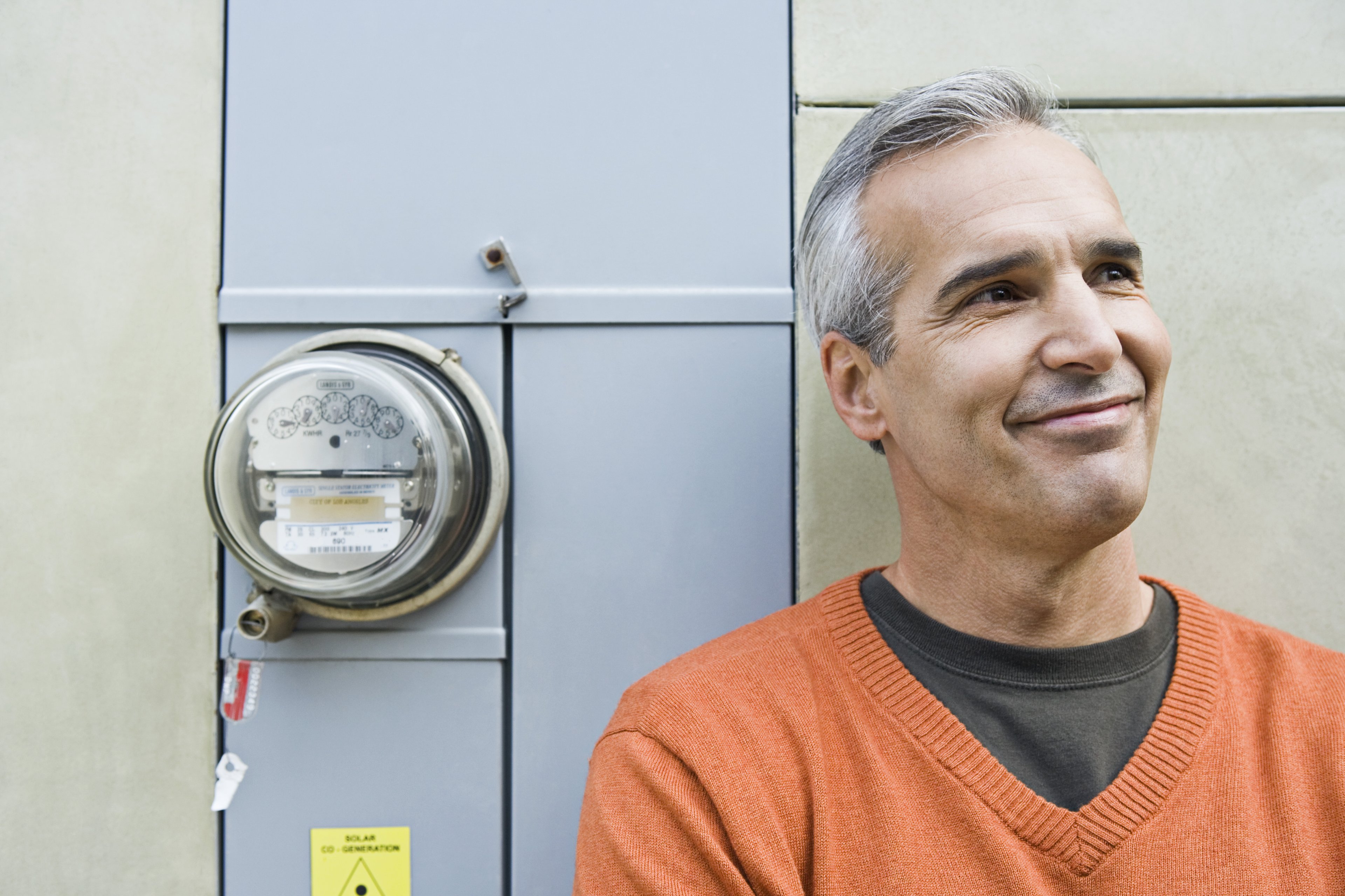 Smiling man standing next to electricity meter on a home. 