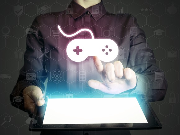 A person touching a video game controller icon that is being projected from a tablet.